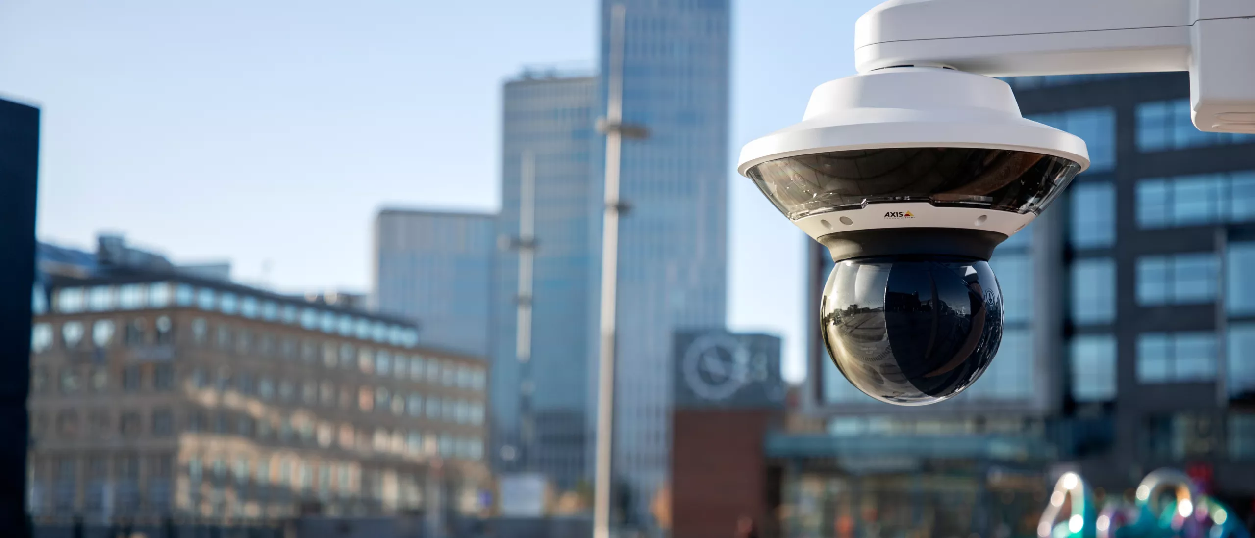 Axis dome camera surveilling over Malmo. Tall buildings in the background with a blue sky.