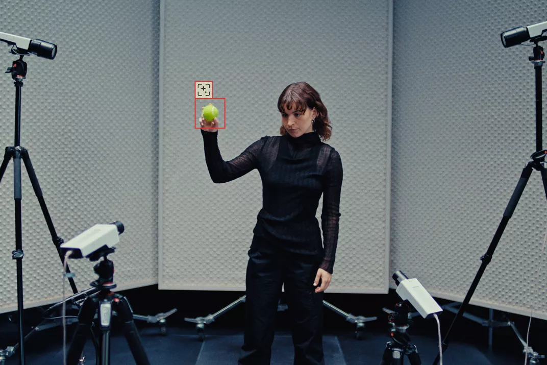 Woman standing in the middle and holding an object in front of four Axis cameras with object detection surrounding her.
